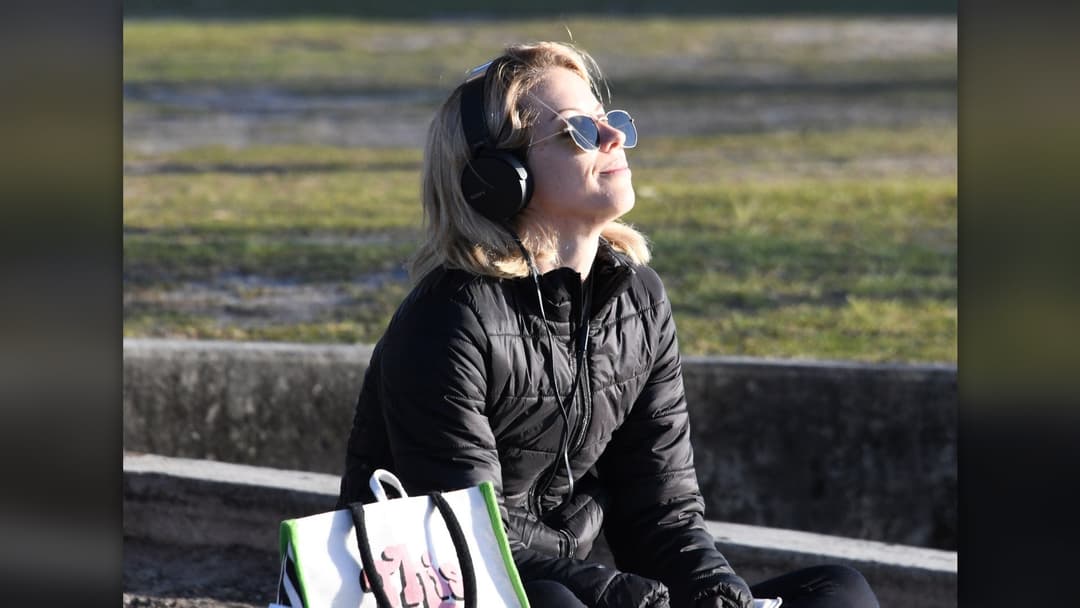 Woman relaxing on a park bench with headphones while her thoughts drift