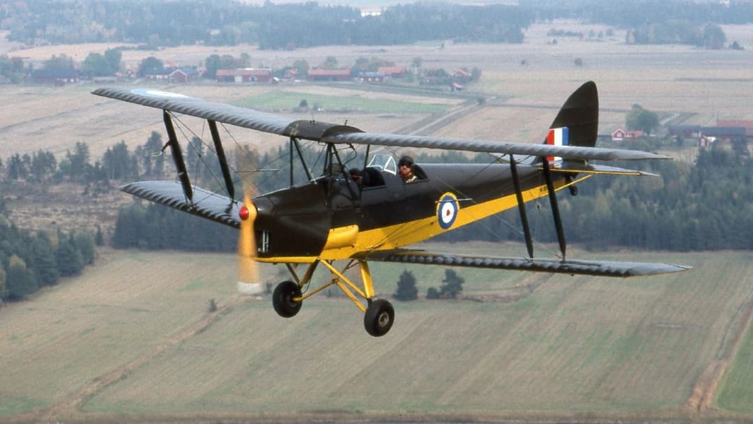 Restored yellow and silver De Havilland DH.82A Tiger Moth biplane trainer parked on an airfield