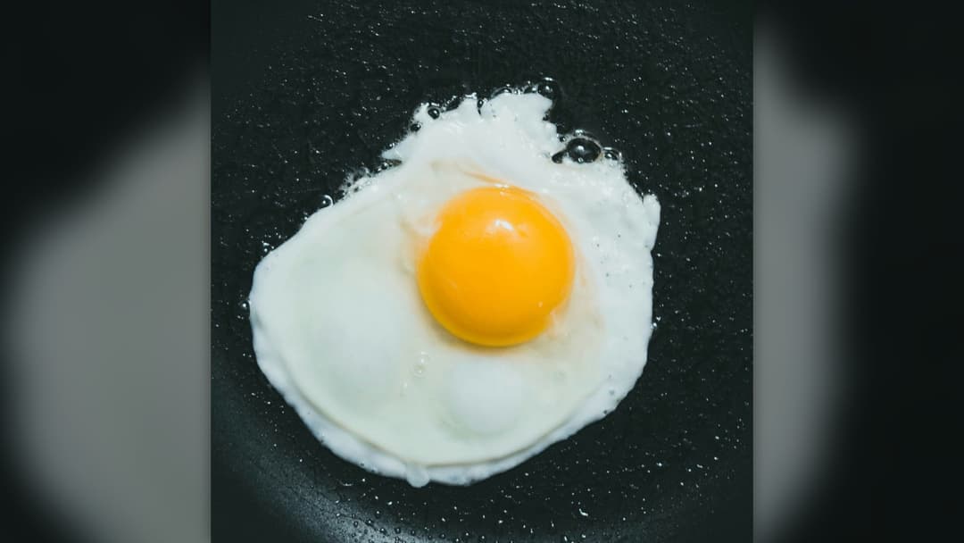 Sunny-side up fried egg with a rich yellow yolk served on a dark textured ceramic plate.