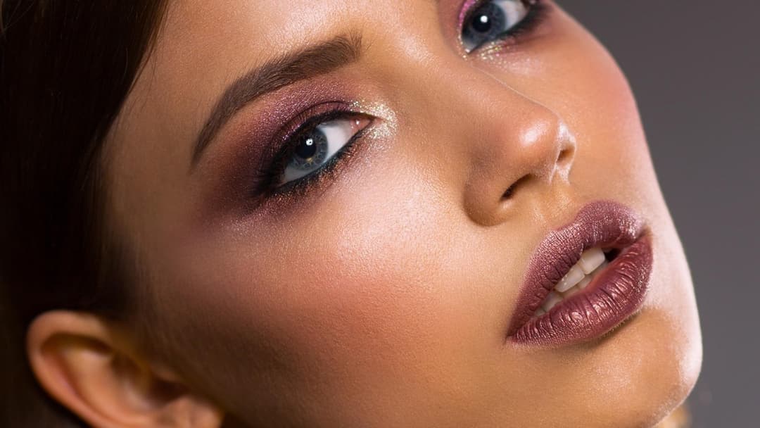 Close-up portrait of a woman with porcelain doll-like skin, bright blue lenses, and sculpted plumped lips