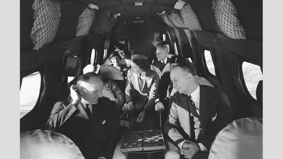 Vintage 1930s air hostess serving passengers inside the cabin of a Boeing 247 airliner
