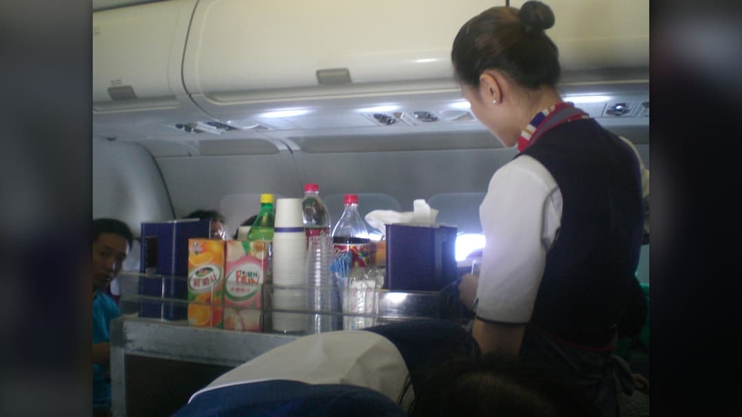 Flight attendant serving economy meal trays to passengers down the aisle of a commercial airliner
