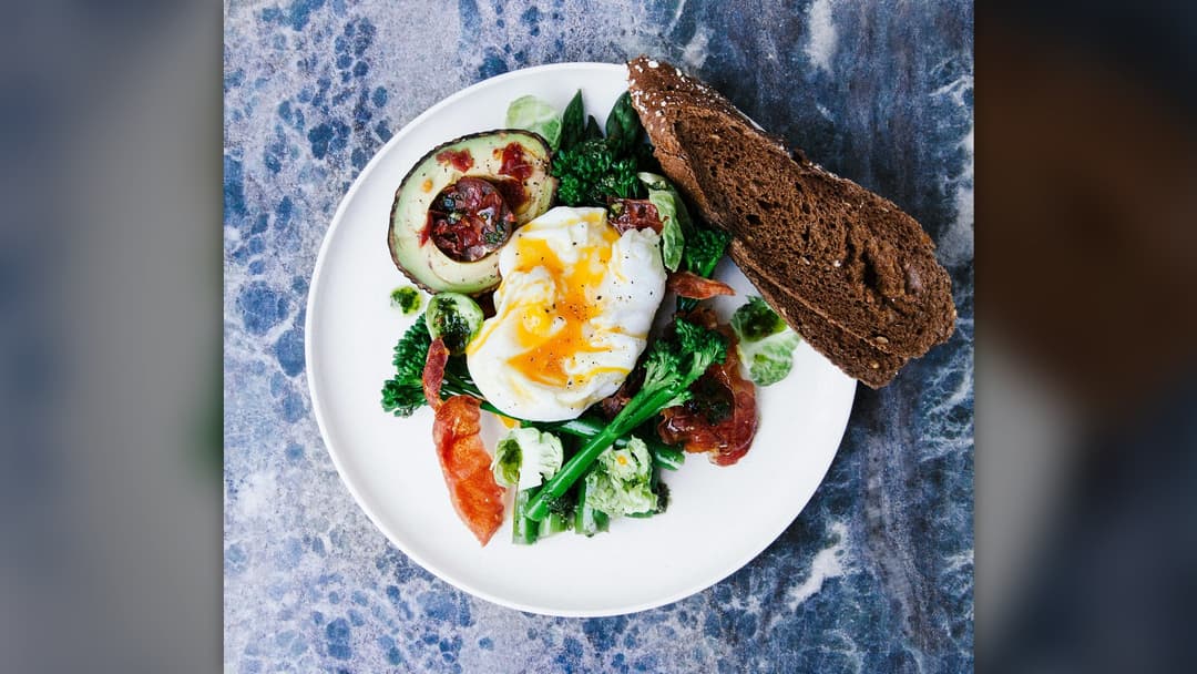 A fresh, balanced salad with greens, vegetables, and poached egg on a white plate.