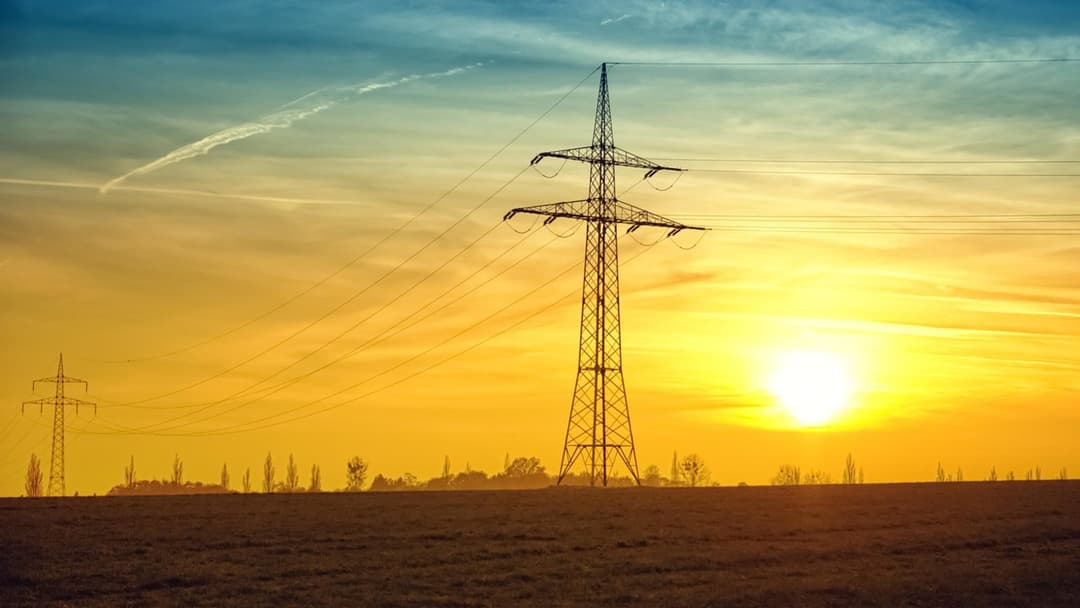 High voltage electrical power grid transmission towers silhouetted at twilight