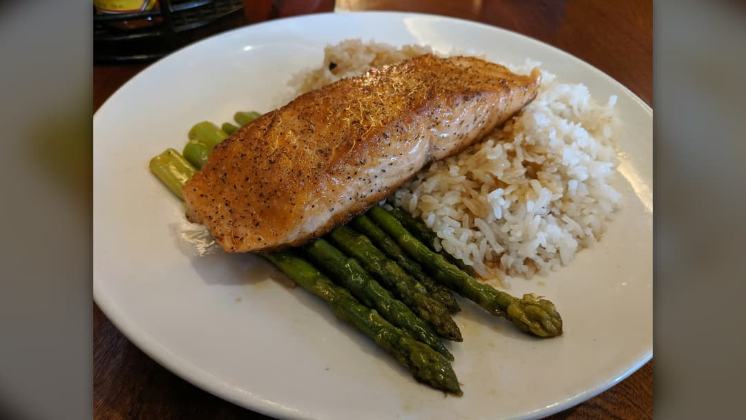 Cooked wild salmon fillet plated over rice with green asparagus