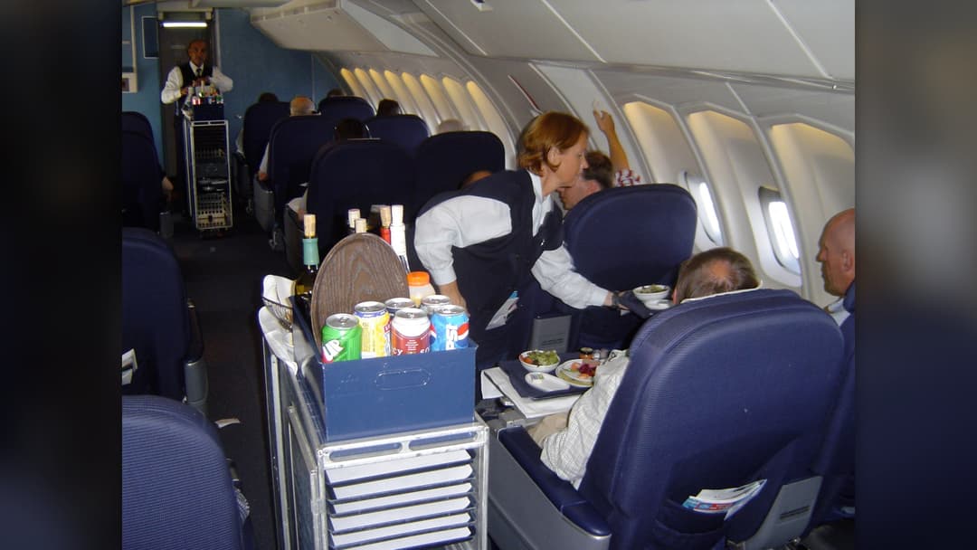 Flight attendant serving meals and beverages to passengers from a trolley in the aircraft cabin