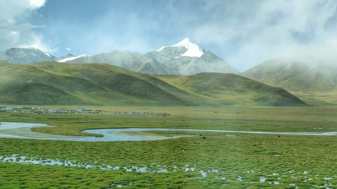 A passenger train on the Qinghai-Tibet Railway crossing snow-dusted mountain plains toward Lhasa.