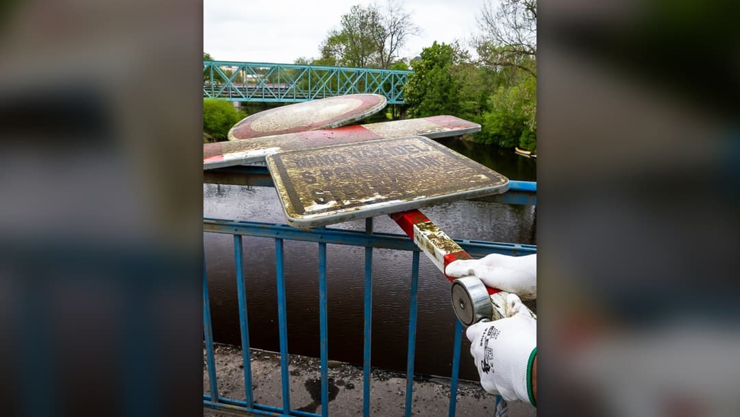 Powerful neodymium magnet on a rope pulling a rusted metal street sign out of a river during magnet fishing