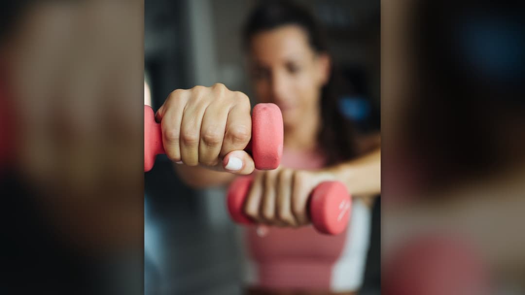 Woman performing dumbbell resistance training during an indoor workout session.