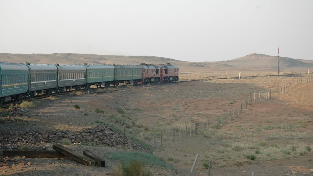 The green Trans-Mongolian Express passenger train stopped at a station platform.
