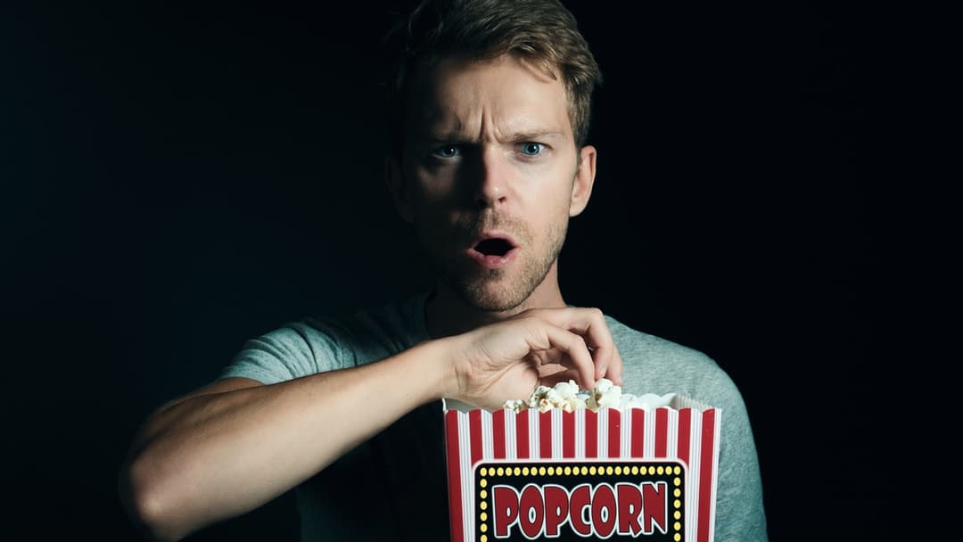 Landscape photograph of a man eating popcorn while watching a scary movie safely at home
