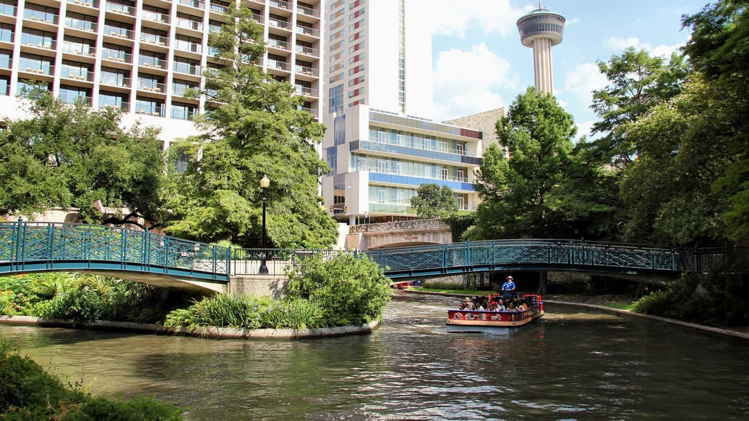 San Antonio River Walk lined with cypress trees and the Tower of the Americas in the background