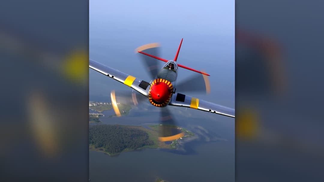 North American P-51D Mustang WWII fighter aircraft in flight over green countryside
