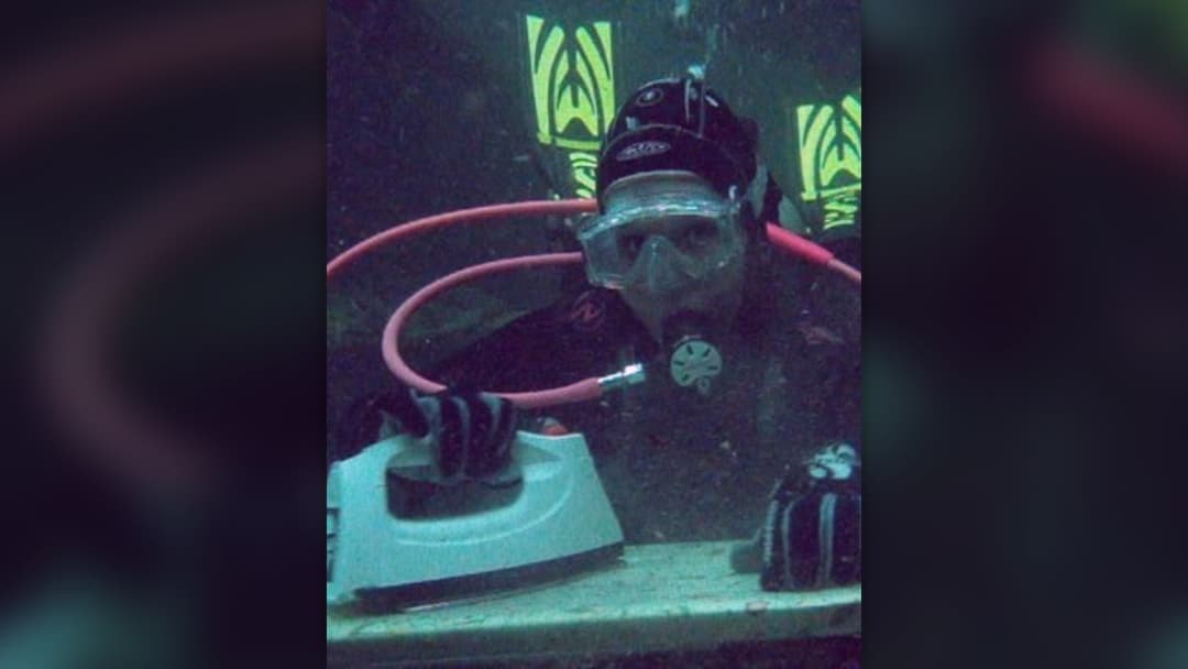 Scuba diver in full underwater gear pressing a shirt on an ironing board on the lake floor