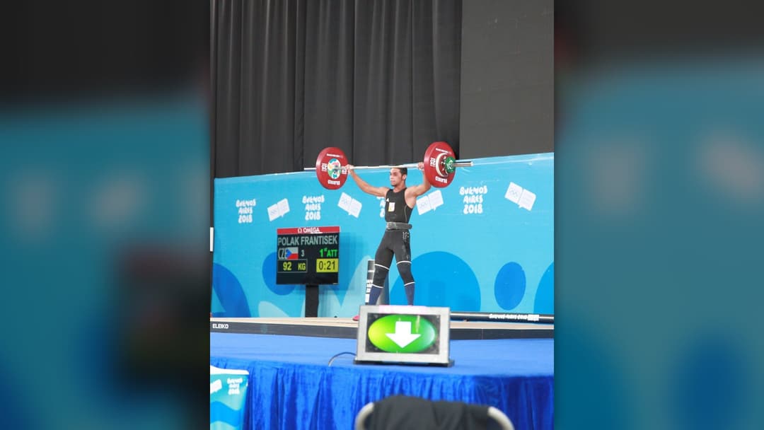 Youth Olympic weightlifter in deep parallel squat position during clean and jerk.
