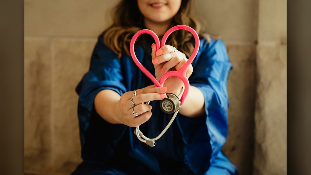Healthcare professional holding a stethoscope formed into a heart shape representing cardiovascular care.