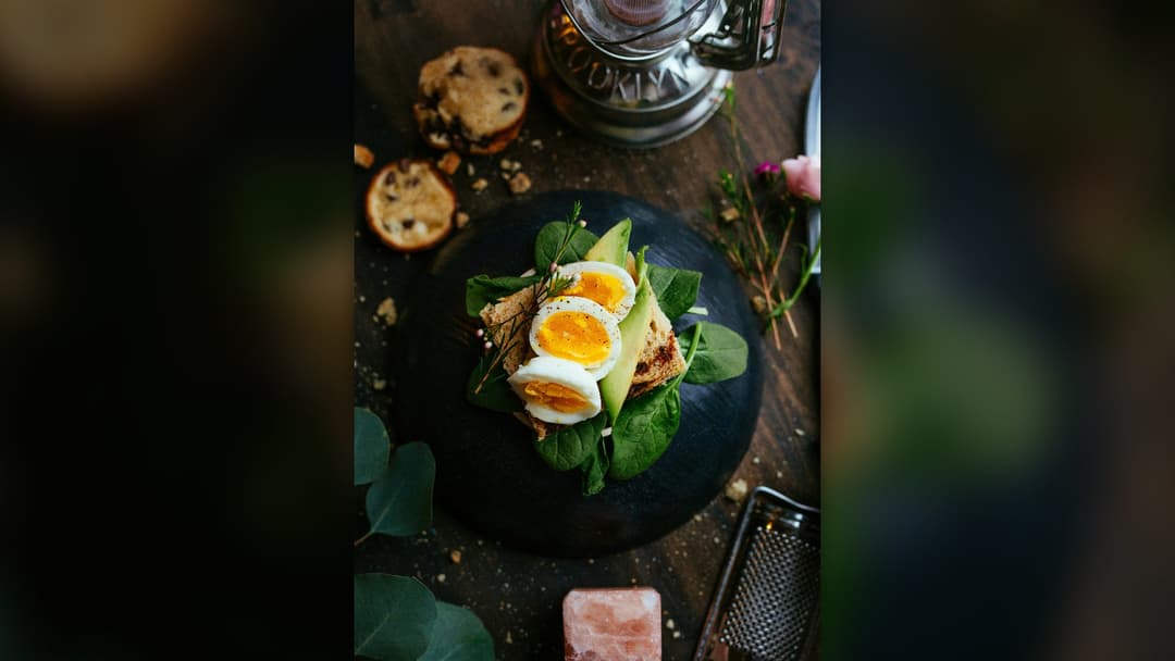 Healthy artisanal whole-grain toast topped with sliced soft-boiled eggs and avocado.