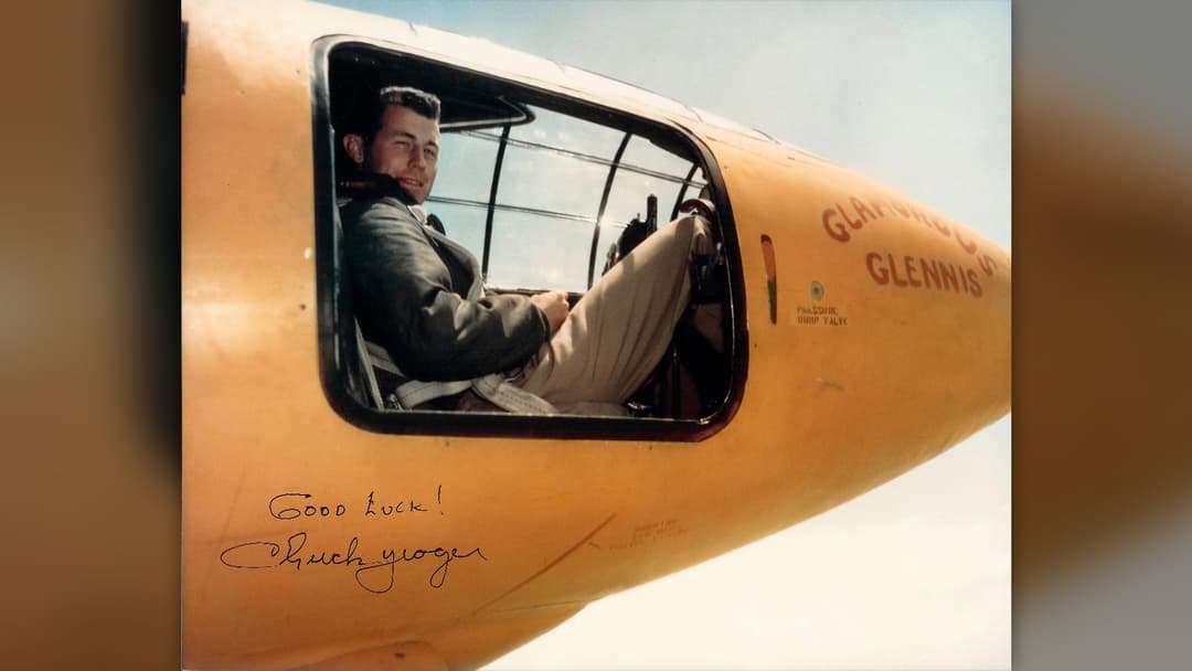 Captain Chuck Yeager seated in the cockpit of the orange rocket-powered Bell X-1 aircraft