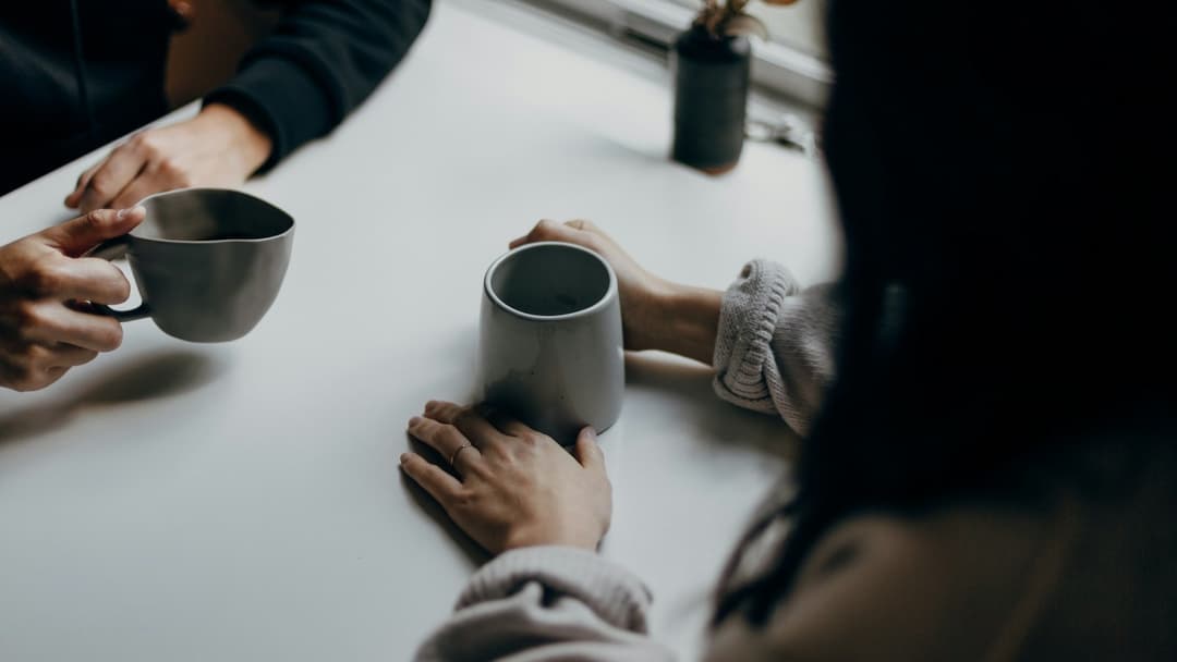 Two people conversing over coffee mugs at a table