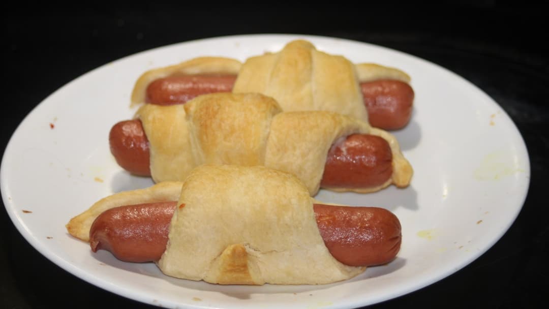 Golden brown pigs in a blanket served on a white plate