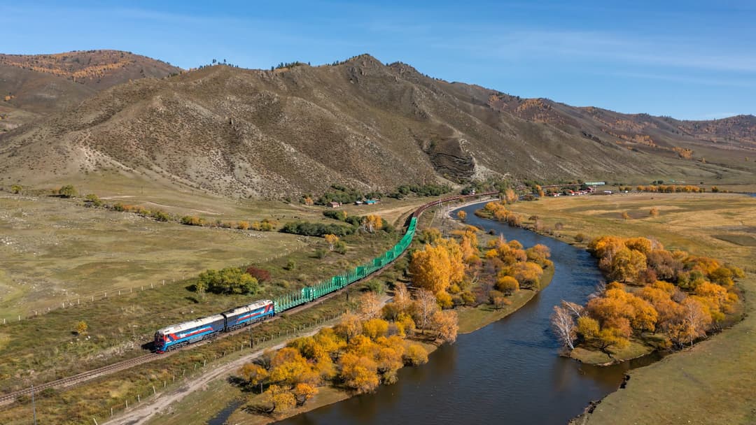 A Mongolian railway locomotive pulling a train across the open green steppe of Mongolia.