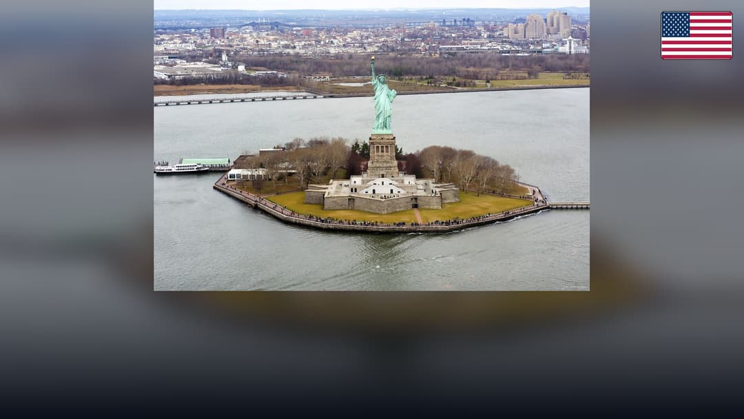 Statue of Liberty on Liberty Island with the American flag in the top right corner.