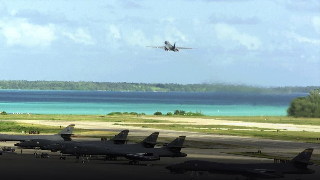 U.S. Air Force B-1B Lancer supersonic strategic bombers parked on the Diego Garcia flightline with another launching over the tropical lagoon.