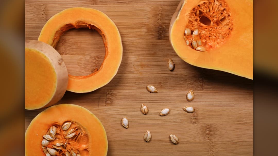 Freshly sliced raw orange pumpkin wedges arranged on a dark brown wooden table.