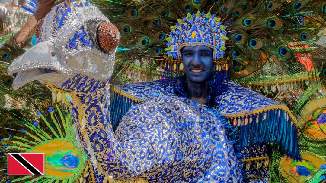 Traditional Carnival masquerader in feathered costume in Trinidad and Tobago with the national flag in the bottom left corner