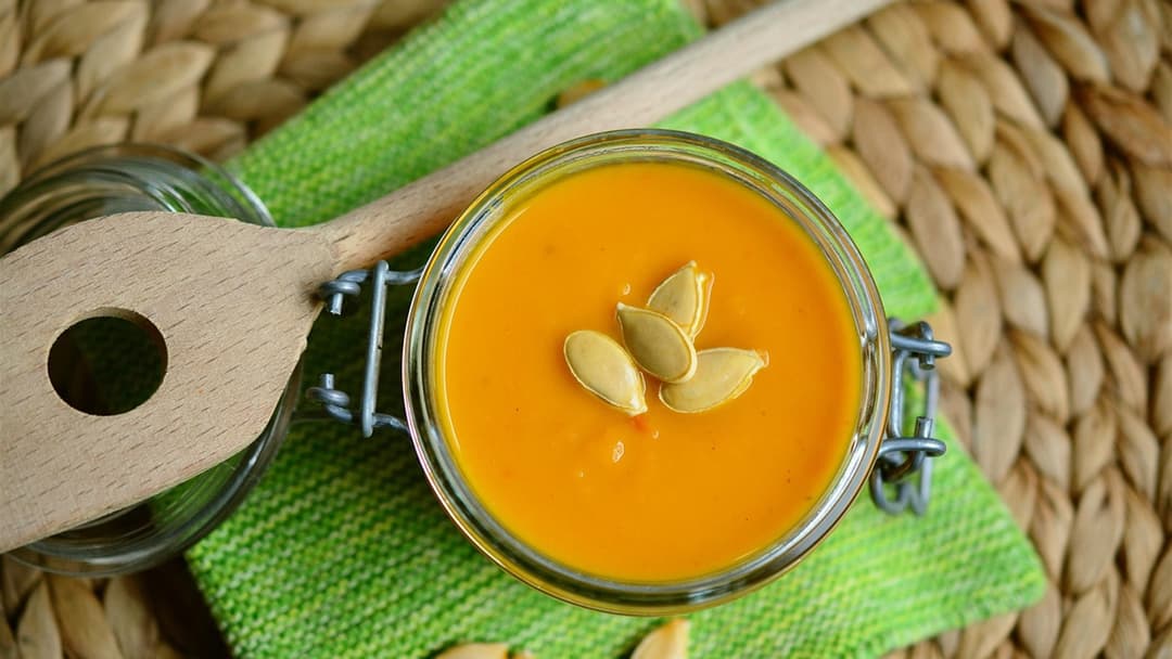 Bowl of warm pumpkin soup topped with roasted pumpkin seeds and green pumpkin seed oil.