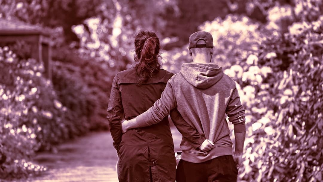 Couple walking down a path with synchronized posture, stride, and arm placement around each other's waists