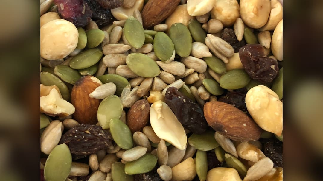 Close-up of trail mix containing almonds, peanuts, green pumpkin seeds, sunflower seeds, raisins, and dried cranberries.