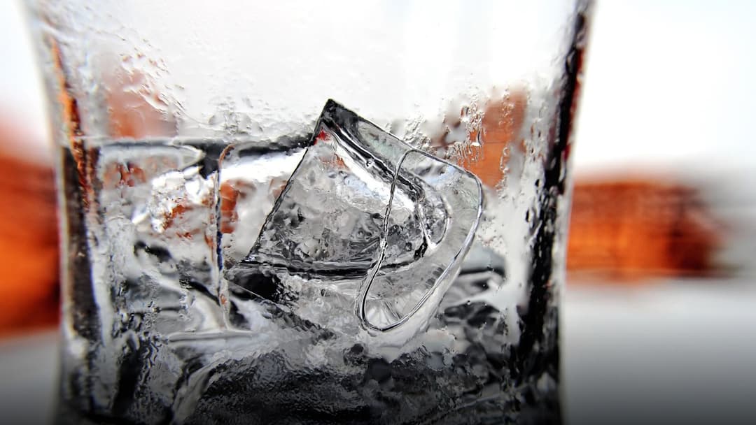 A clear beverage glass packed to the brim with glistening ice cubes.