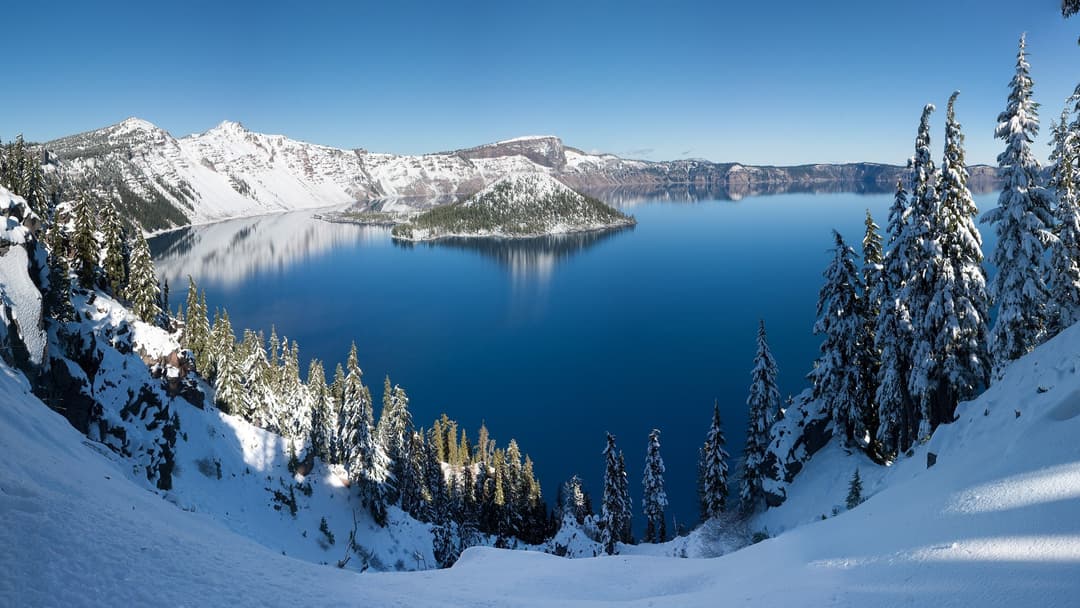 Snow-covered caldera rim and Wizard Island cinder cone in Crater Lake, Oregon.