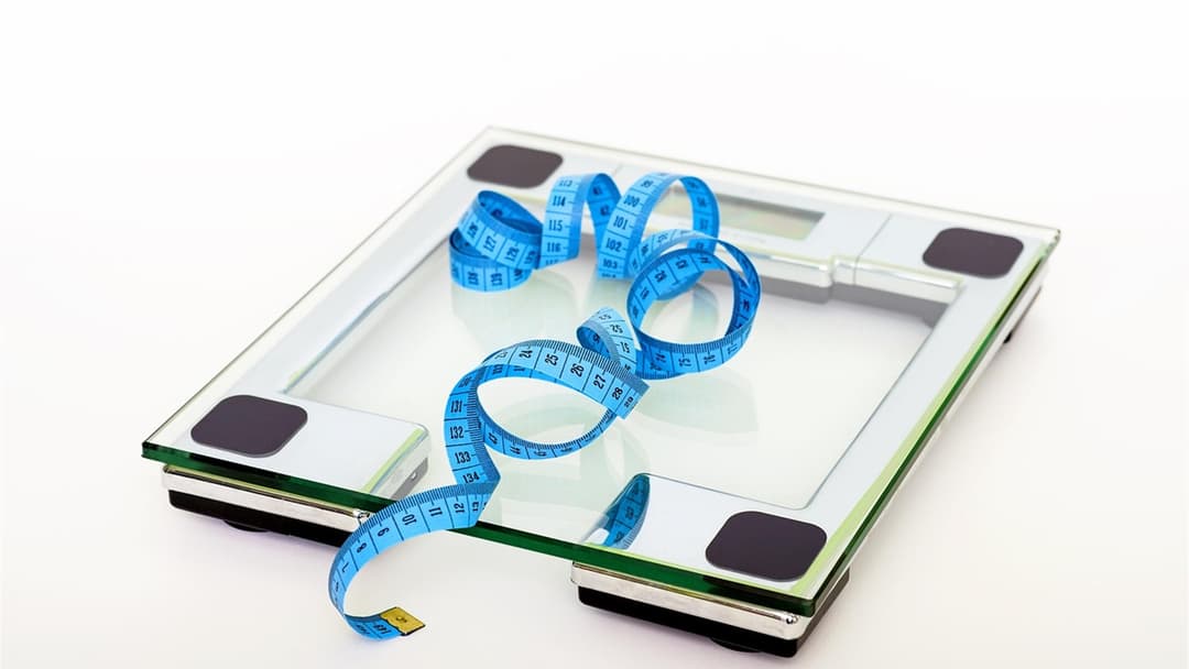 Fitness bathroom scale with a green measuring tape wrapped around it for weight tracking.