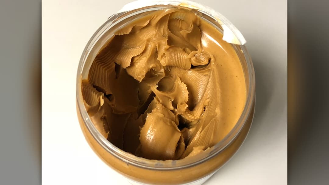 Top view of an open jar of creamy golden-brown peanut butter showing knife swirls.