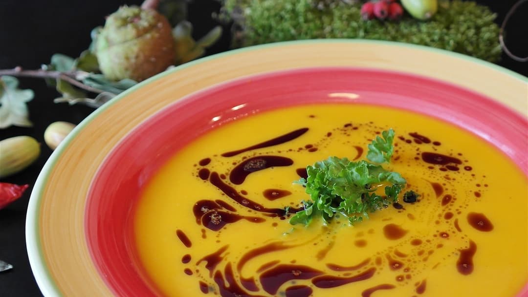 Bowl of creamy orange Hokkaido pumpkin puree soup garnished with herbs.