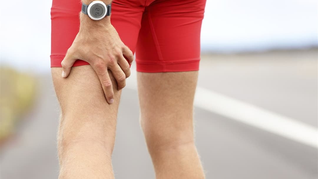 Outdoor runner holding his upper leg muscle during an exercise recovery stretch.