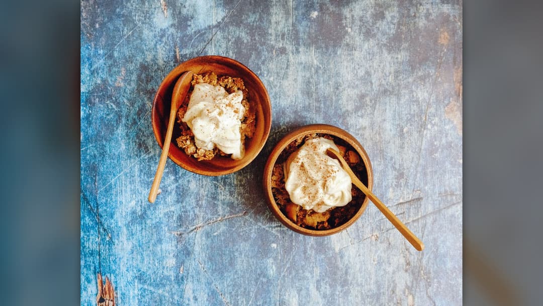 Two wooden bowls filled with crunchy baked oat granola and topped with white yogurt and cinnamon.
