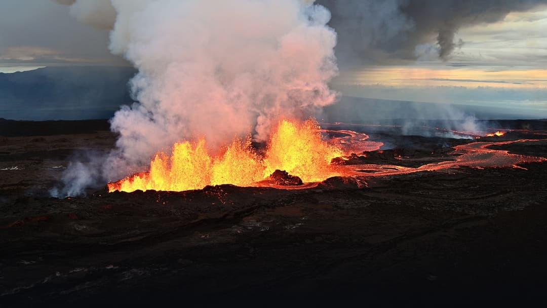 High-altitude morning vista of Mauna Loa erupting fissure with soaring orange-gold lava fountains, glowing lava rivers, and illuminated volcanic steam plume.