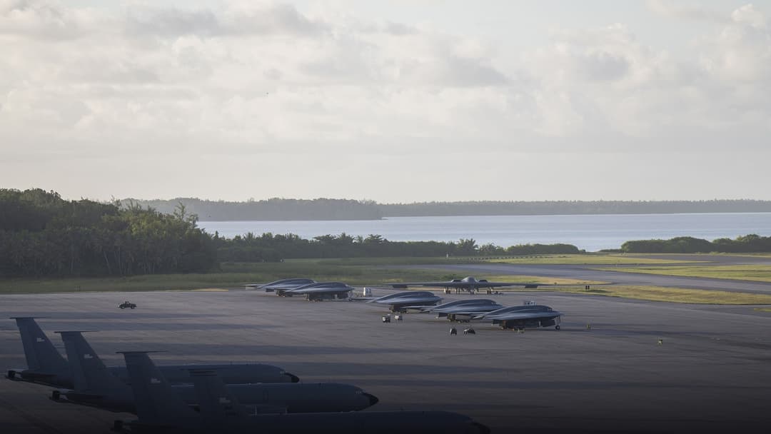 A military transport aircraft on the Diego Garcia flightline with airmen silhouetted against airfield lights.