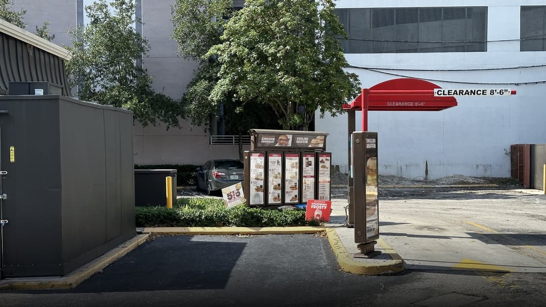 A fast-food drive-thru ordering lane with menu board, speaker post, and vehicle clearance barrier.