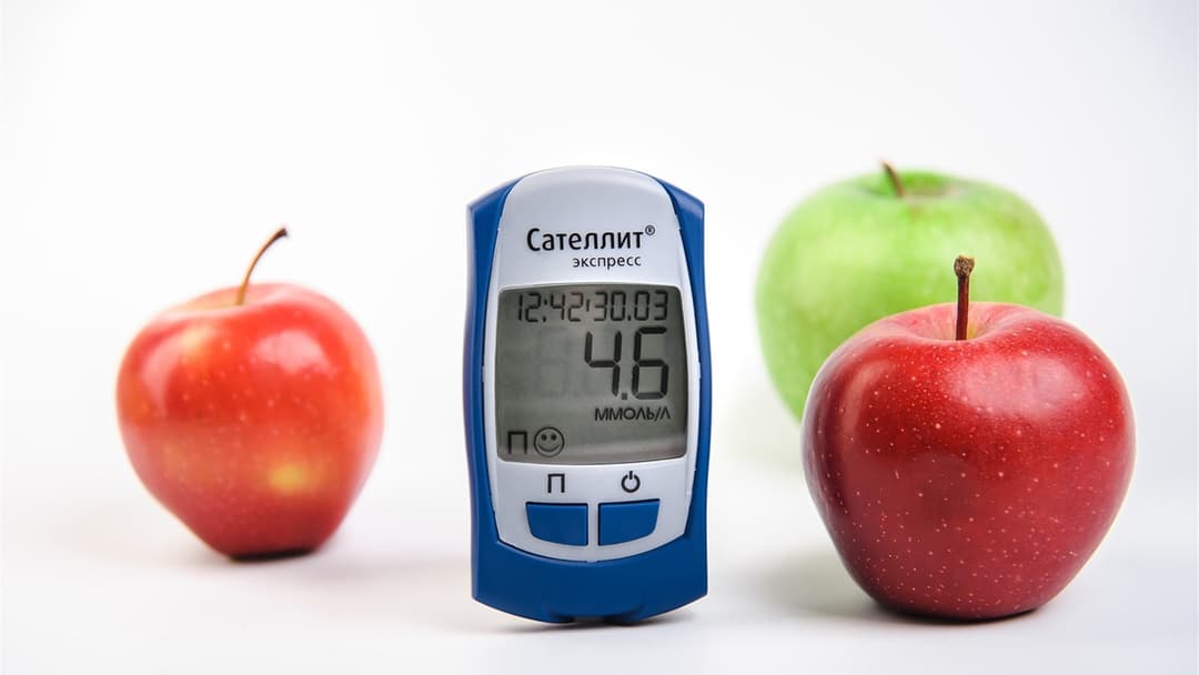 Blood glucose meter resting beside fresh produce on a wooden surface.