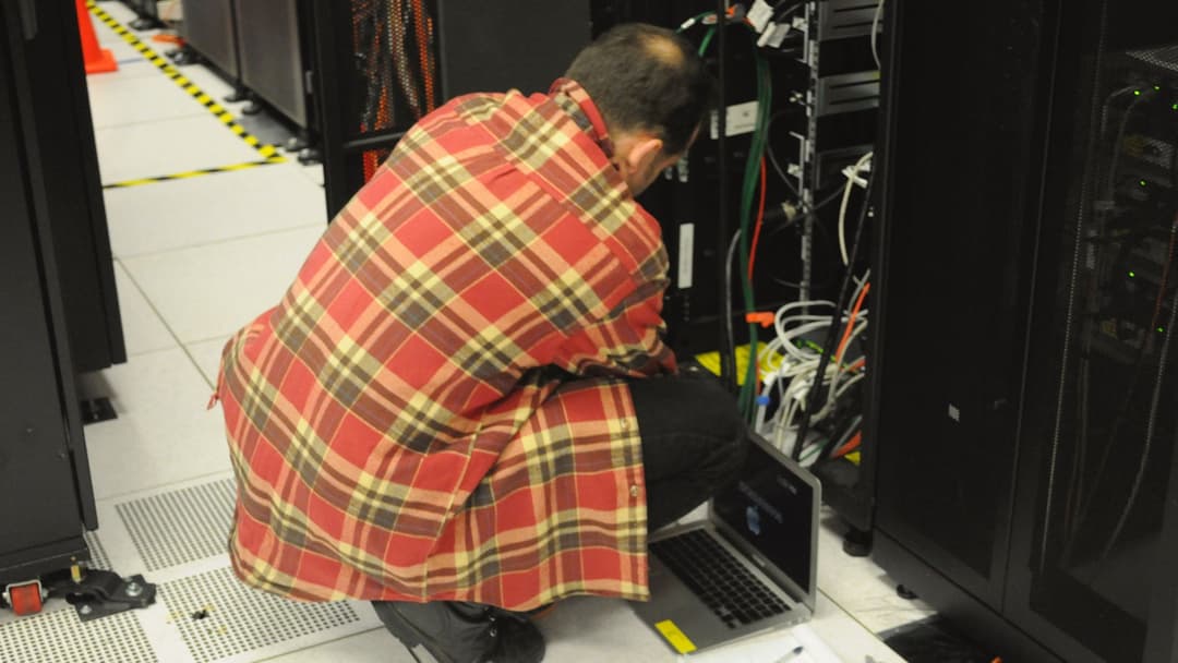 Data center systems engineer working with a laptop beside server racks at NERSC