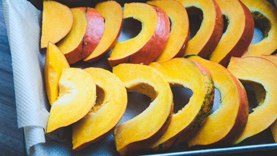 Bright orange cut pumpkin slices arranged neatly on a dark baking tray.