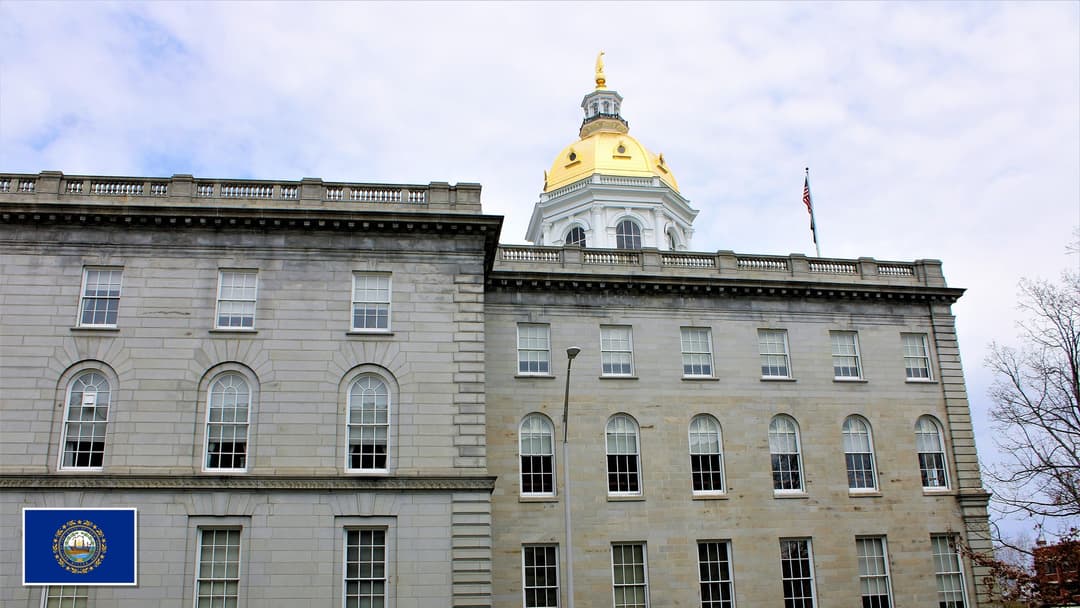 New Hampshire State House in Concord, New Hampshire with the New Hampshire state flag in the bottom left corner