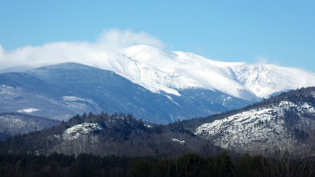 The snow-capped summit of Mount Washington rising dramatically above winter alpine foothills.