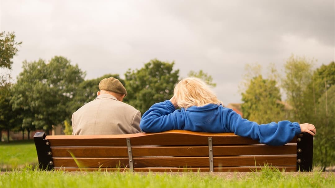 Elderly married couple sitting side by side on a park bench after decades of marriage