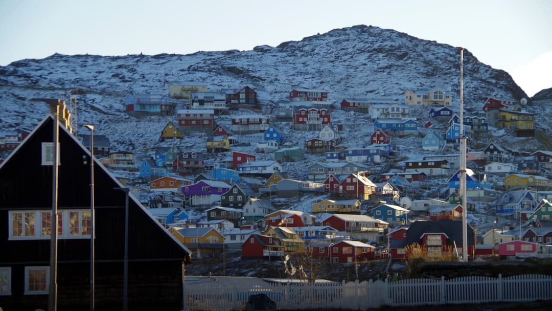 Vivid yellow, red, and blue wooden houses perched across rocky coastal hills overlooking the harbor in Qaqortoq.