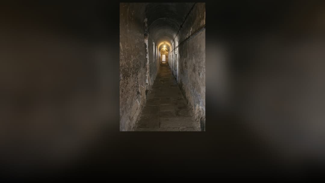 A secure high-walled prison corridor and cellblock walkway.
